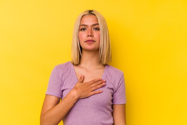 Jovem venezuelana isolada em fundo amarelo, fazendo um juramento, colocando a mão no peito.