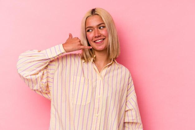 Jovem venezuelana isolada na parede rosa, mostrando um gesto de chamada de telefone móvel com os dedos.