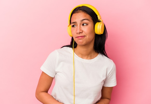 Jovem venezuelana ouvindo música isolada em fundo rosa confusa, sente-se em dúvida e insegura.