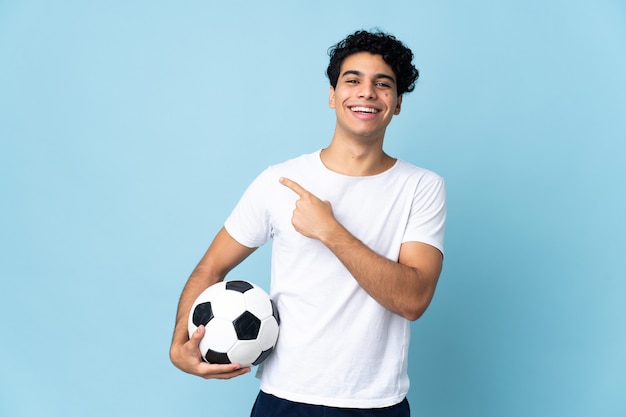 Jovem venezuelano em azul com bola de futebol e apontando para a lateral