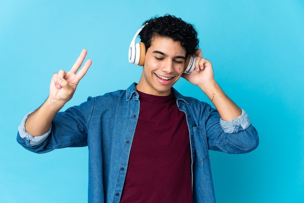 Jovem venezuelano isolado em uma parede azul ouvindo música e cantando