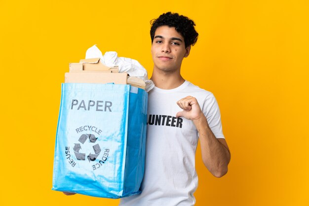 Jovem venezuelano segurando uma sacola de reciclagem cheia de papel para reciclar orgulhoso e satisfeito