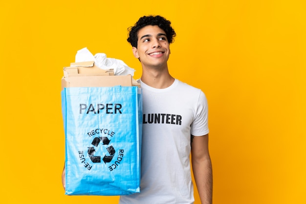 Jovem venezuelano segurando uma sacola de reciclagem cheia de papel para reciclar pensando em uma ideia enquanto olha para cima