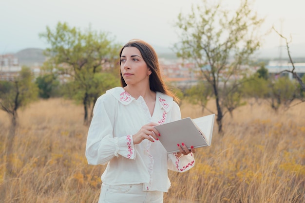 Jovem vestida de branco lendo um livro em um prado ao pôr do sol