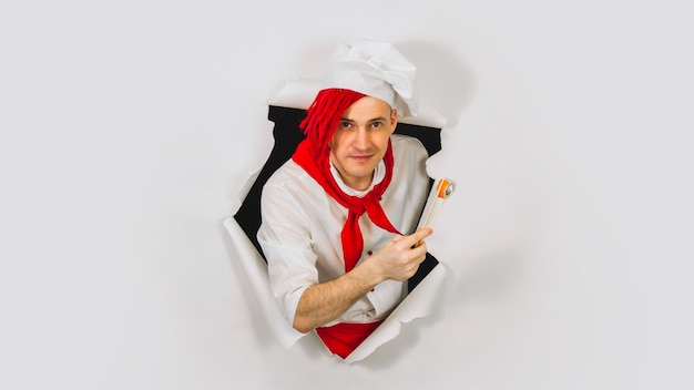 Jovem vestido de chef segurando pauzinhos com rolo Cozinheiro masculino com rolo de sushi apetitoso saindo do buraco de fundo branco Conceito de fast food e takeaway