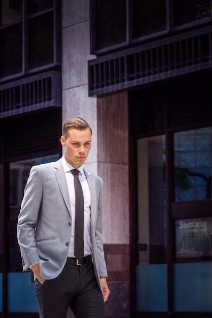 Jovem vestindo blazer cinza camisa branca gravata preta caminhando na rua olhando para baixo pensando