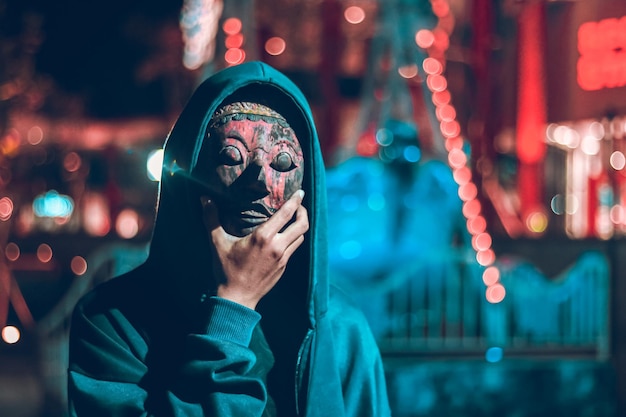 Jovem vestindo máscara de pé contra luzes iluminadas à noite