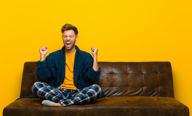 Jovem vestindo pijama, olhando extremamente feliz e surpreso, comemorando o sucesso, gritando e pulando