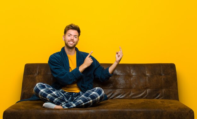 Jovem vestindo pijama sorrindo alegremente e apontando para o lado e para cima com as duas mãos, mostrando o objeto no espaço da cópia