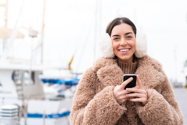 Jovem vestindo regalos de inverno ao ar livre enviando uma mensagem com o celular