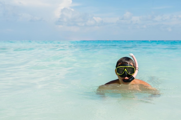 Jovem vestindo uma máscara de mergulho contra um céu azul claro e oceano turquesa