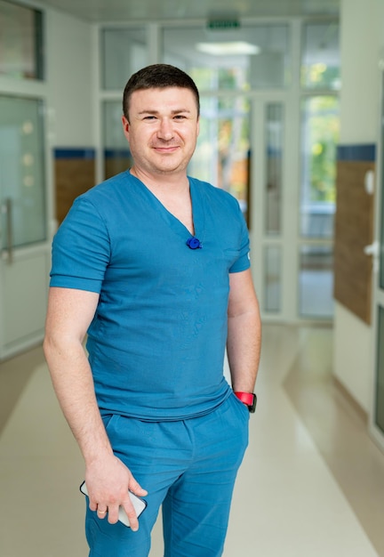 Jovem vestindo uniforme azul posando para a câmera no hospital moderno. Bonito especialista médico de uniforme.