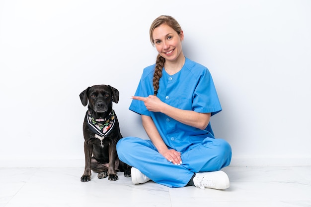 Jovem veterinária com cachorro sentado no chão isolado no fundo branco e apontando para ele