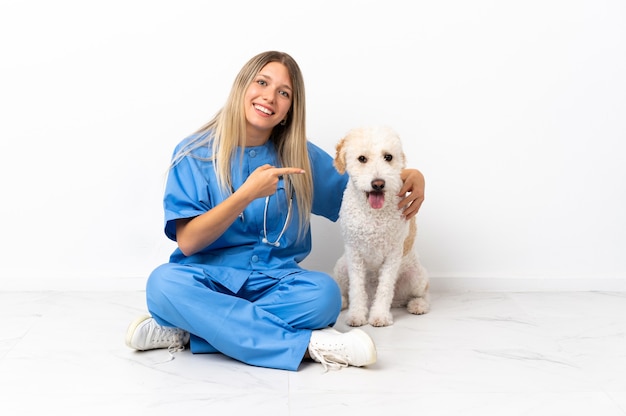 Jovem veterinária com o cachorro sentado no chão apontando o dedo para o lado