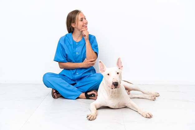 Jovem veterinária inglesa sentada no chão com cachorro olhando de lado