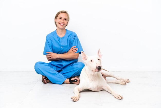 Jovem veterinária inglesa sentada no chão com cachorro sorrindo muito