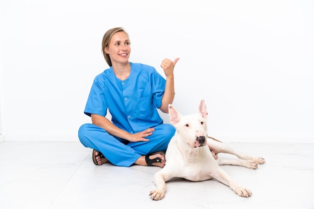 Jovem veterinária inglesa sentada no chão com um cachorro com o polegar para cima porque algo bom aconteceu