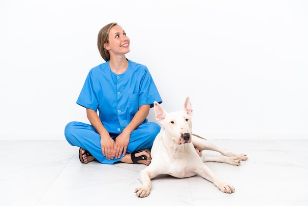 Jovem veterinária inglesa sentada no chão com um cachorro olhando para cima enquanto sorri