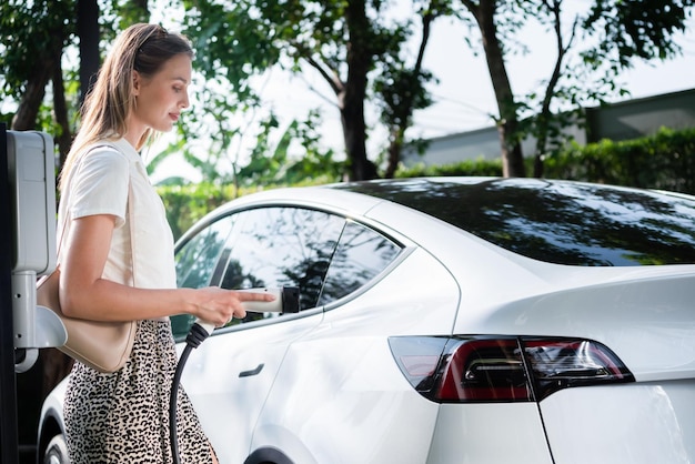 Jovem viaja com carro elétrico EV carregando no jardim ao ar livre da cidade verde sustentável no verão Estilo de vida de sustentabilidade urbana por energia recarregável limpa verde de entranhas de veículos elétricos BEV