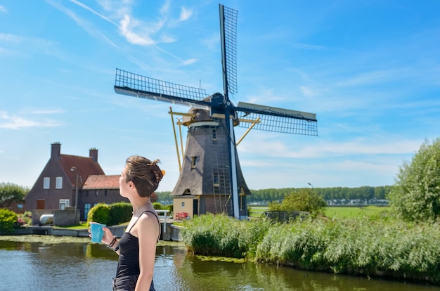 Jovem viaja de férias na Holanda olhando moinho de vento holandês de barcaça no canal