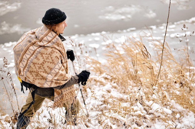 Jovem viajando com varas de caminhada de mochila Caminhada de inverno na floresta Turista em caminhada no inverno na floresta natureza selvagem sazonal conceito de bushcraft cara ativo e esportivo em roupas quentes