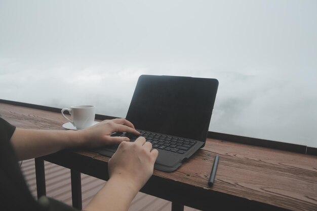 Jovem viajante autônomo usando chapéu em qualquer lugar, trabalhando on-line usando um laptop e apreciando a vista das montanhas