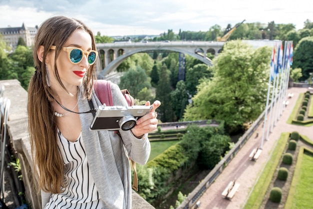 Jovem viajante com fotocâmera, apreciando a bela vista da cidade no vale verde com ponte e jardim na cidade de Luxemburgo