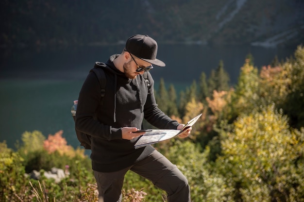 Jovem viajante com mapa e mochila relaxante ao ar livre com montanhas rochosas no fundo