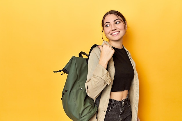 Foto jovem viajante com sua mochila aponta com o dedo polegar longe rindo e despreocupado