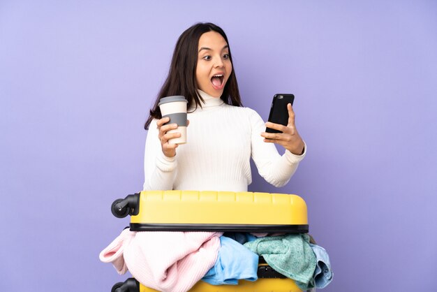 Jovem viajante com uma mala cheia de roupas segurando café para levar e um celular