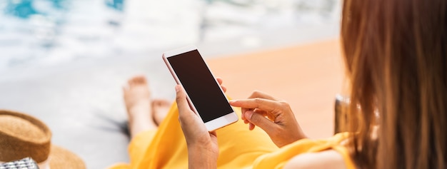 Jovem viajante relaxando e usando um telefone celular ao lado da piscina de um hotel durante as férias de verão