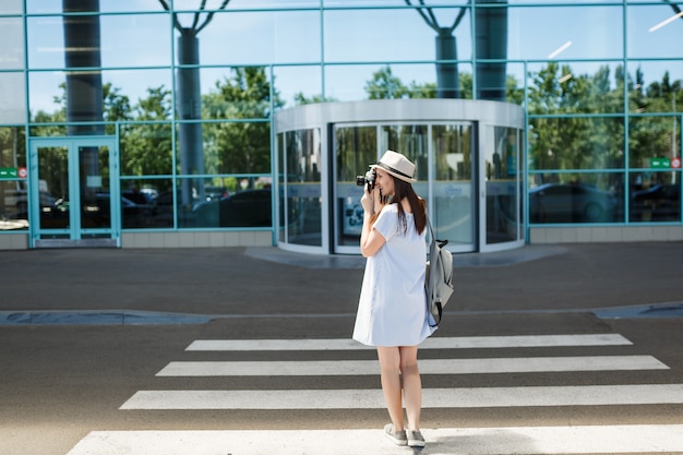 Jovem viajante turista com mochila tira fotos em câmera fotográfica vintage retrô na faixa de pedestres do aeroporto internacional