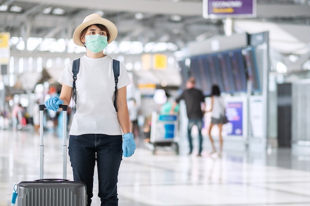 Jovem viajante usando máscara facial e luva nitrílica segurando alça de bagagem no terminal do aeroporto, proteção contra infecção por coronavirus (covid-19). novo conceito normal e bolha de viagens