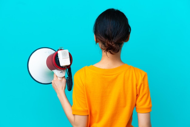 Jovem vietnamita isolada em fundo azul segurando um megafone e na posição traseira