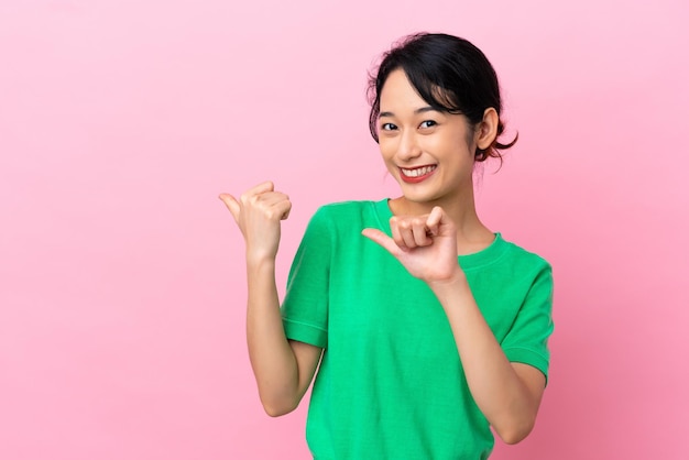 Jovem vietnamita isolada em fundo rosa apontando para o lado para apresentar um produto