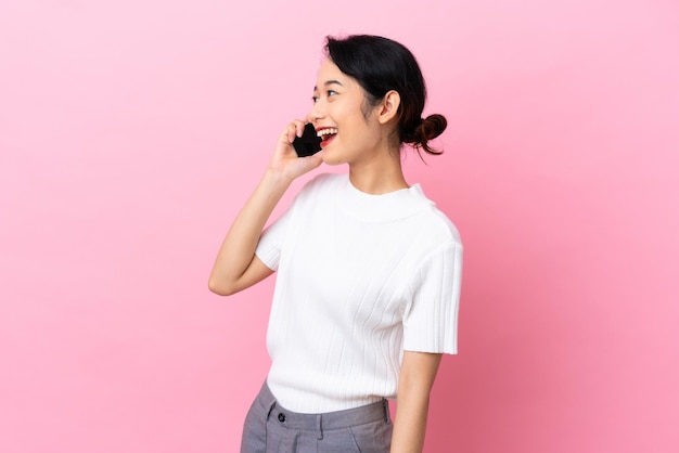 Jovem vietnamita isolada em fundo rosa, mantendo uma conversa com o celular