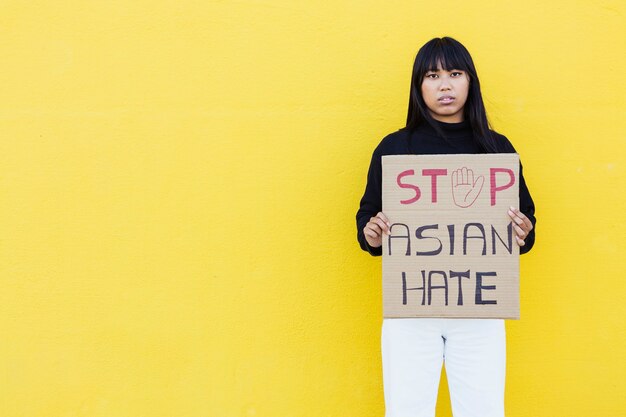 Jovem vietnamita protestando por direitos iguais em pé contra uma parede amarela durante a campanha "Pare a luta contra o ódio na Ásia