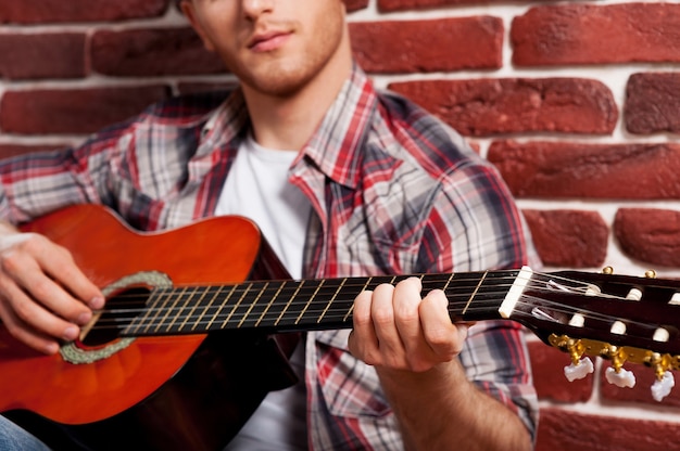 Jovem virtuoso. Close de um jovem bonito tocando violão enquanto se inclina para a parede de tijolos