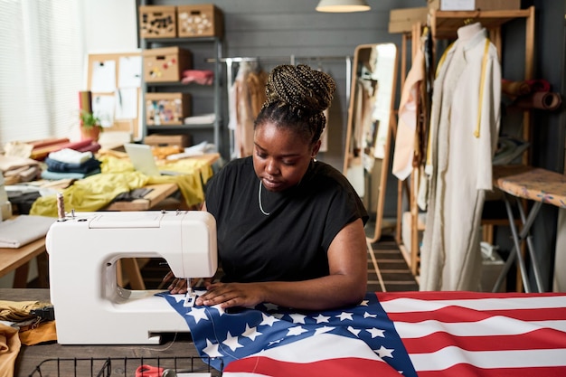 Jovem voluntária afro-americana costurando bandeira dos EUA na máquina elétrica