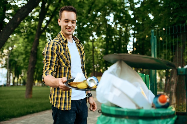 Jovem voluntário coloca lixo em lata de plástico no parque, voluntariado