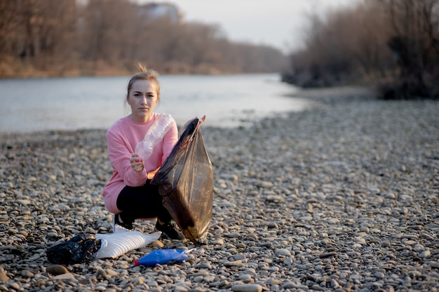 Jovem voluntário do sexo feminino coletando lixo no rio