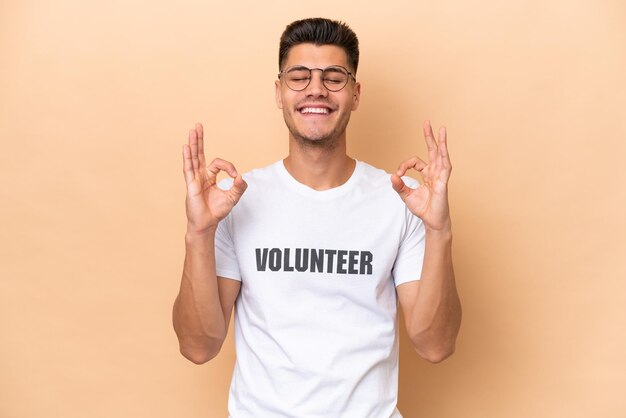 Jovem voluntário homem caucasiano isolado em fundo bege em pose zen