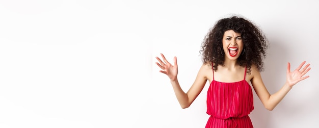 Foto jovem zangada com cabelo encaracolado usando vestido vermelho gritando e tendo uma discussão olhando com ha