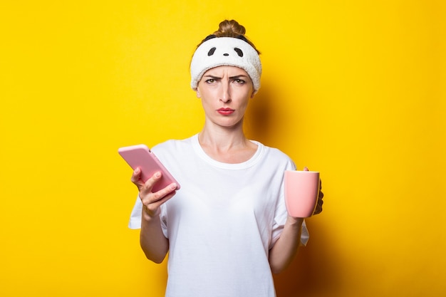 Jovem zangada em uma bandagem com um telefone e uma xícara de café em um fundo amarelo