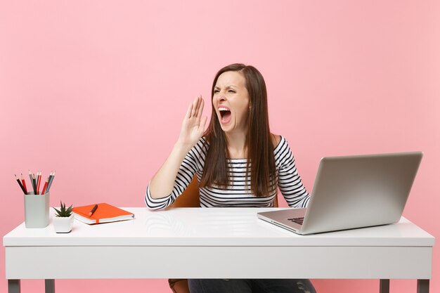 Jovem zangada gritando enquanto trabalhava em um projeto sentada no escritório com um laptop pc contemporâneo