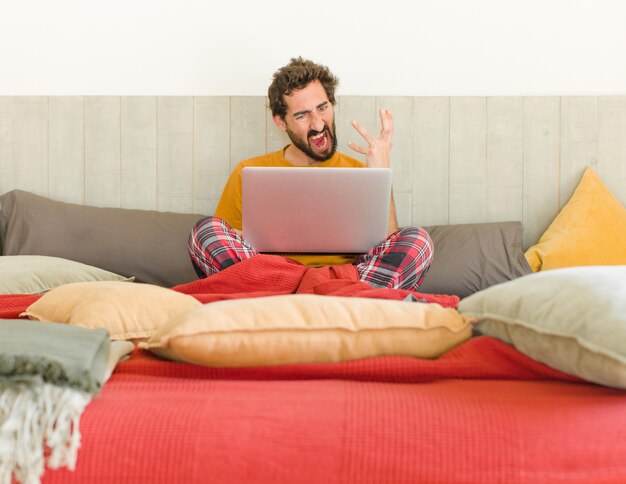 Jovem zangado com um laptop na cama