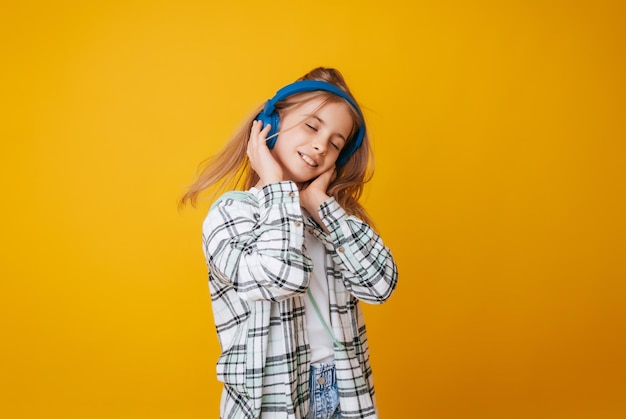 Una joven de 1113 años con auriculares escucha música y baila en el estudio con un fondo amarillo