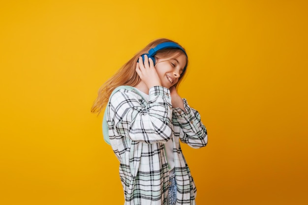 Una joven de 1113 años con auriculares escucha música y baila en el estudio con un fondo amarillo