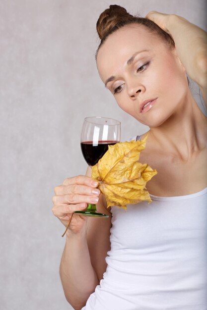 Foto una joven de entre 30 y 40 años mantiene hojas de arce secas y un vaso de vino tinto cerca de su cara.