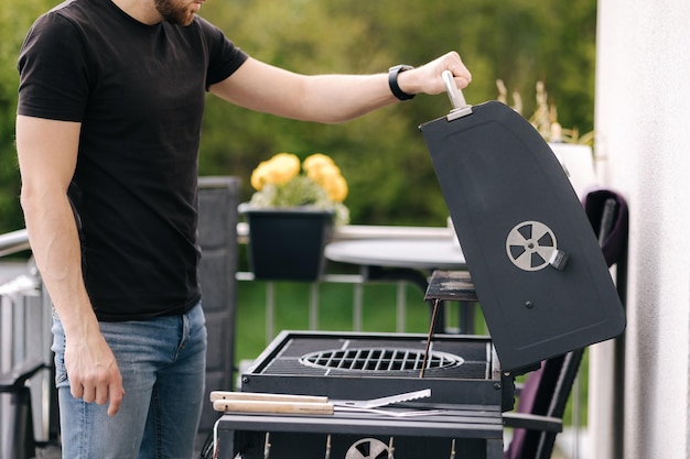 Joven abierto barbacoa parrilla y preparándose para limpiar el comienzo de la fiesta de verano en el patio trasero